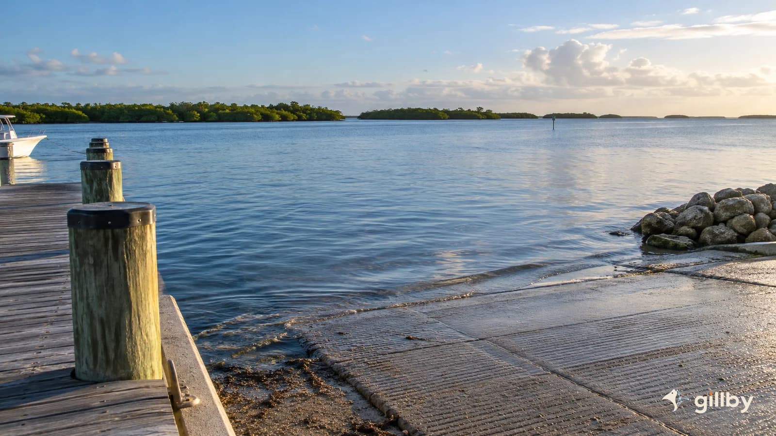 Quiet concrete boat ramp and dock beside blue coastal water with Gillby logo